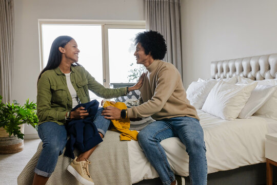 Diverse couple sorting laundry in modern bedroom, with yellow sweater and dark clothing - Powered by Adobe