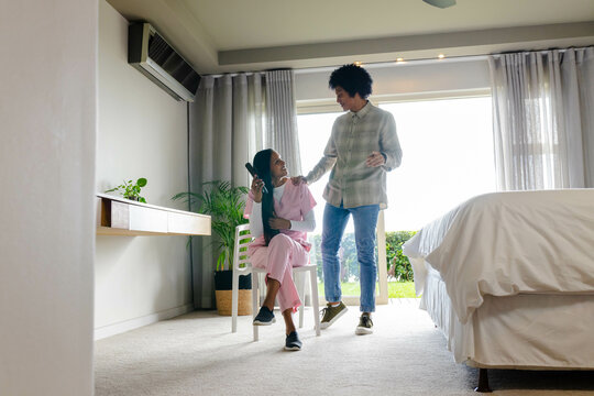 Talking diverse couple sitting and standing in modern bedroom, with hairbrush and potted plant