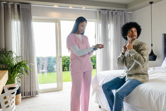Standing diverse caregiver and patient chatting at bedside, with smartwatch and sliding door
