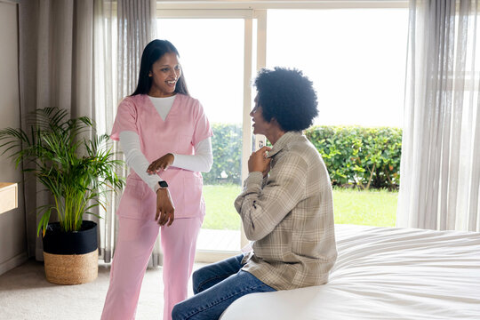 Asian Indian nurse and male patient discussing smartwatch use in bedroom, with sliding door view - Powered by Adobe
