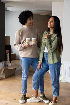 Holding two takeaway coffee cups, diverse couple unpacking in bright living room, with moving boxes