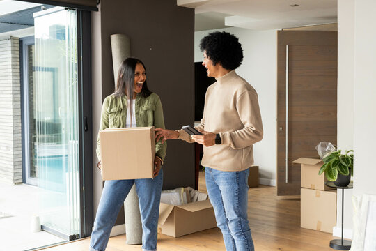 Using handheld scanner, delivery worker and Indian woman moving cardboard boxes in living room