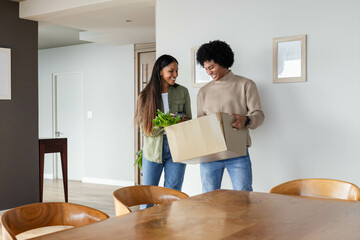 Unpacking Diverse couple holding cardboard box with fresh leafy greens in modern dining area