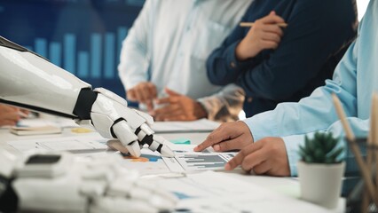 A robot hand interacts with human colleagues during a business meeting. They analyze various charts...