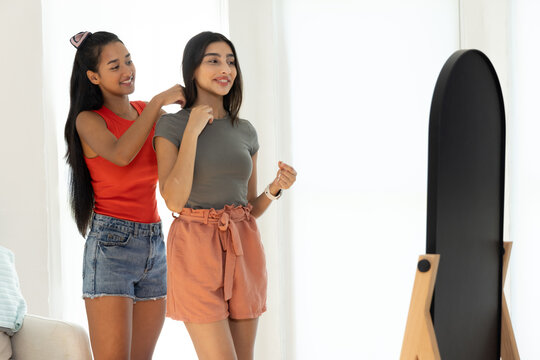 Adjusting necklace diverse female friends standing in living room, with mirror, copy space