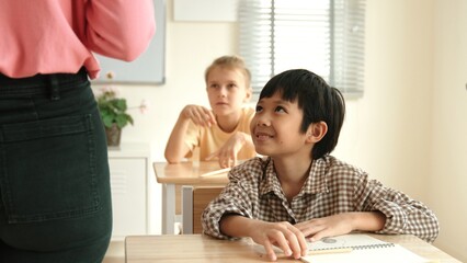 Asian elementary student looking at teacher while attend in classroom. Diverse smart student sitting at classroom while listening teacher explain about classwork or test. Education concept. Pedagogy.