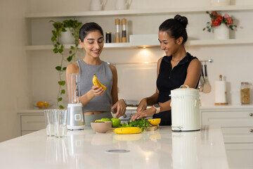 Chopping Diverse female friends prepping smoothie ingredients on kitchen island, with blender jar