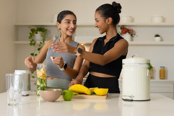 Cutting bananas Diverse female friends preparing smoothie on kitchen island, with blender and apple
