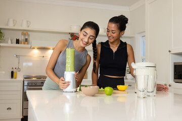 Blending Diverse female friends preparing smoothie in modern home kitchen, with countertop blender
