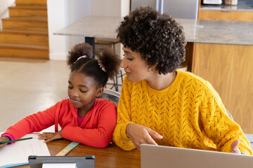 Teaching Diverse mother and daughter working on homework at kitchen table, with laptop and notebook
