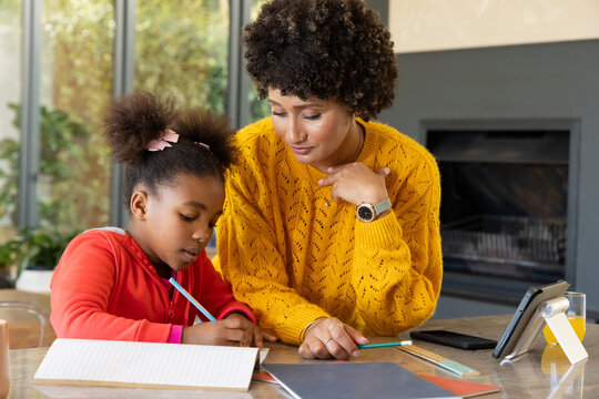 Diverse mother and daughter working together at home, with notebook and colored pencils