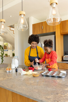 Baking mother and daughter mixing batter at kitchen island, with glass bowl and whisk