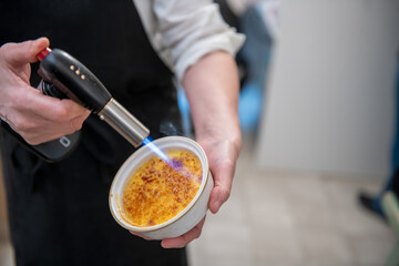 Chef preparing creme brulee with torch flame in elegant kitchen setting