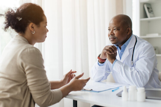Friendly conversation between African American doctor and woman patient during medical visit, therapist man listening attentively young female during appointment in clinic