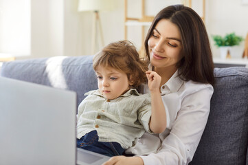Mother and little kid son spending time using laptop computer, babysitter sitting together at home,...