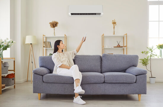 Woman switching on air conditioner at home, blowing warm, cold air room temperature control, adjust for optimal device performance, home environment, providing ideal climate using remote control