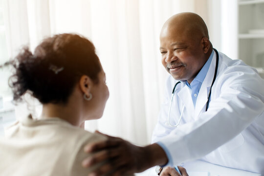 Support Concept. Portrait of mature black male doctor tapping patting patients shoulder for empathy and encouragement during appointment in clinic. General practitioner cheering woman at office