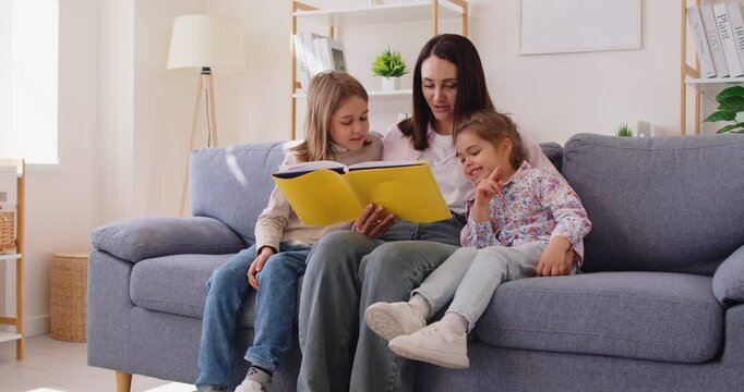 Happy mother with kids spends leisure reading book together, relaxing on sofa at home, fostering family bonding in a familiar scene with focus on connection and engagement in the activity.