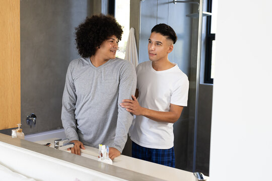 Standing Diverse male friends washing hands at home bathroom sink, with toothbrush holder