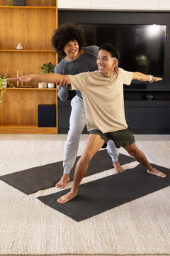 Practicing yoga Diverse men holding wide lunge on black mats in living room, with shelves, TV