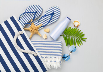 Blue beach bag with summer accessories on color background, top view