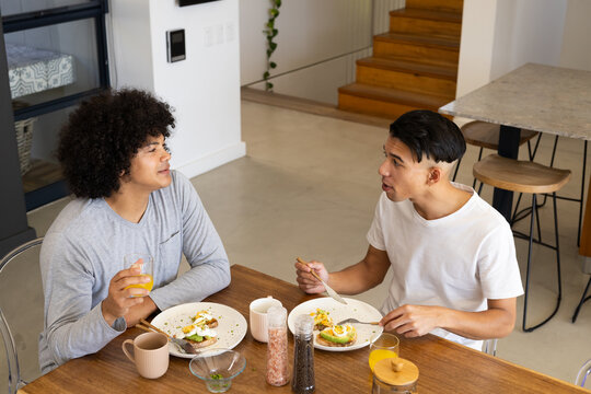 Diverse male friends eating avocado toast at dining table in modern home, with orange juice - Powered by Adobe