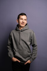 A Casual Portrait Featuring a Man Dressed in a Gray Hoodie Set Against a Vibrant Purple Background