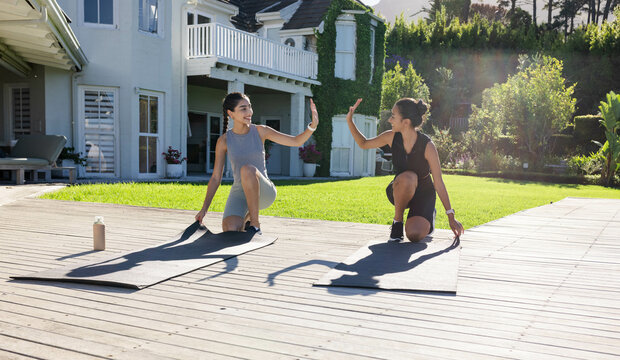 High-fiving diverse female friends kneeling on suburban deck, with black yoga mats and water bottle