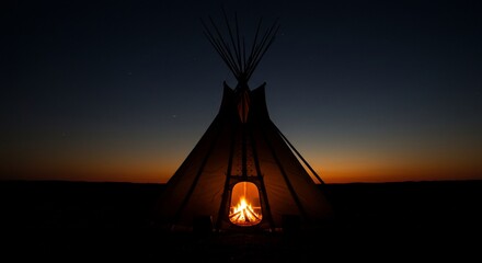 Illuminated teepee against twilight horizon