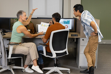 Collaborating Diverse coworkers examining data at desk in open-plan office, with monitors, coffee