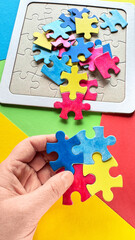 Autism World Awareness Day concept, hand holding colorful puzzle pieces with scattered pieces