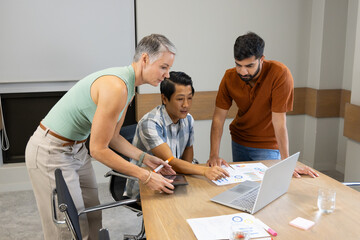 Collaborating Diverse coworkers leaning over desk in modern conference room, with tablet and charts