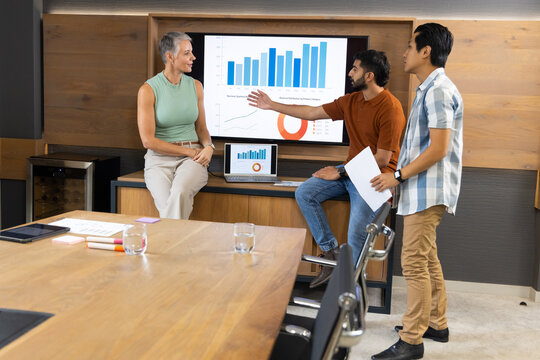 Diverse coworkers discussing chart data in wood-paneled conference room, with papers and laptop