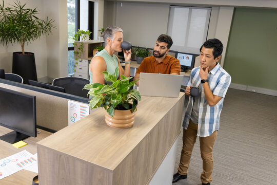 Diverse coworkers discussing sales data in open-plan office around reception desk, with laptop