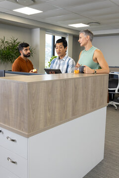 Diverse coworkers reviewing info at wooden reception desk, with tablet and fruit bowl