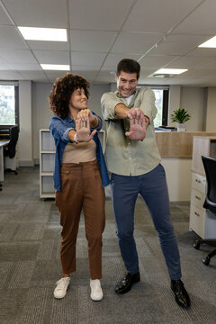 Stretching Diverse coworkers extending arms forward in open-plan office, with computer monitors
