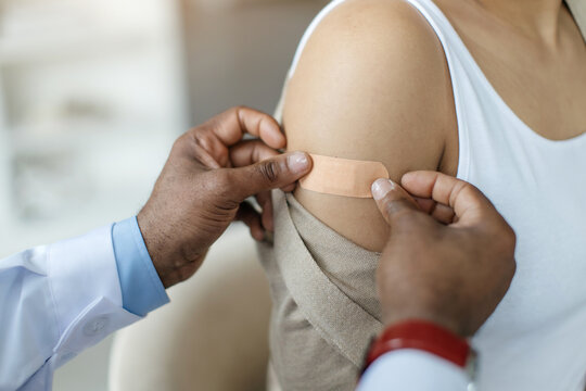 Doctor Applying Plaster On Arm Of Black Female Patient After Vaccine Shot, Closeup Shot Of Unrecognizable Medical Worker Using Adhesive Bandage For Young African American Woman After Vaccination