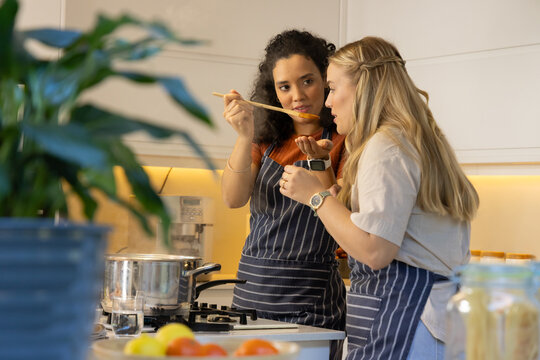 Cooking Diverse female friends tasting soup at kitchen island, with wooden ladle and steel pot