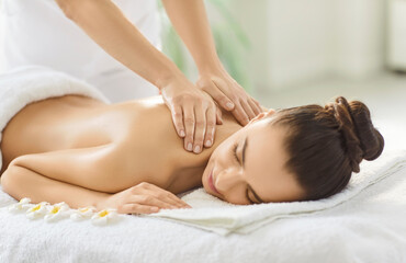 Cropped image of unknown massage therapist doing back massage for woman client, helping to reduce pain or muscle tension. Brunette woman enjoying massage and calm atmosphere in spa salon