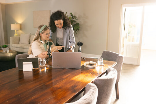 Collaborating diverse coworkers recording podcast at home workspace, with microphones and laptop