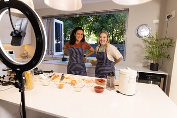 Smiling Diverse female friends cooking on kitchen island, with ring light and chopped vegetables