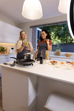 Cooking Diverse female friends preparing pasta at kitchen island, with olive oil and spaghetti jar