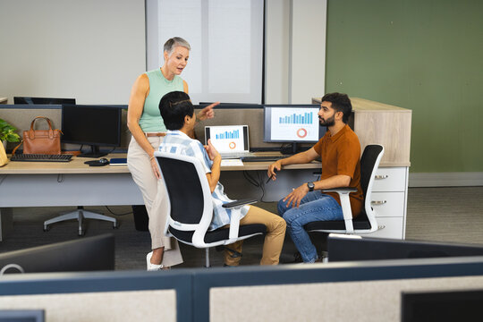 Collaborating Diverse coworkers analyzing bar and pie charts in modern office, with monitors