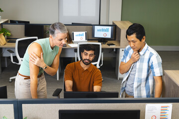 Collaborating Diverse coworkers analyzing charts at workstation in open-plan office, with cubicles