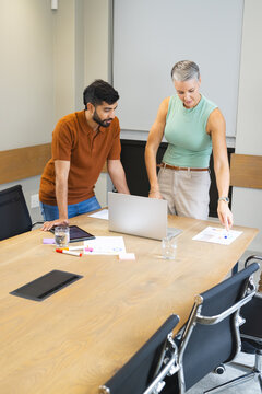 Leaning Diverse coworkers analyzing data in meeting room, with silver laptop and printed charts