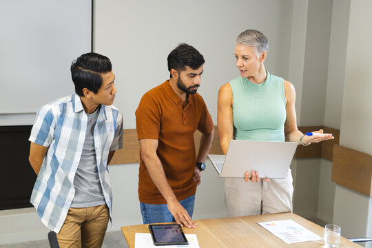 Diverse colleagues discussing and reviewing charts on laptop in modern meeting room, with tablet
