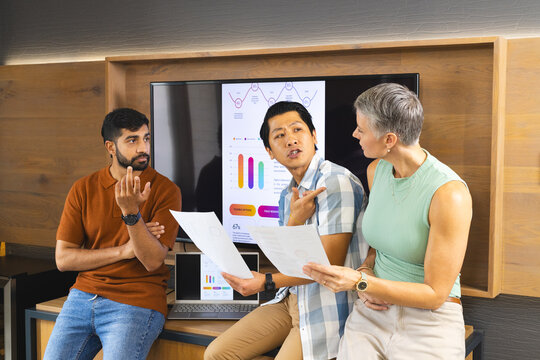 Discussing Diverse coworkers analyzing data on flat-screen at office desk, with printed documents