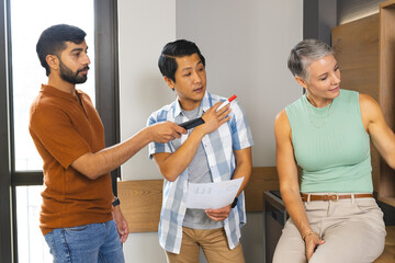 Diverse coworkers discussing strategy in modern office meeting area, with printed chart and pointer