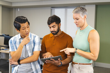 Collaborating instructor with students navigating tablet in computer lab, with desktop computers