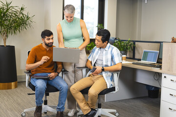 Collaborating Diverse coworkers reviewing data on laptop in office, with tablet and phone